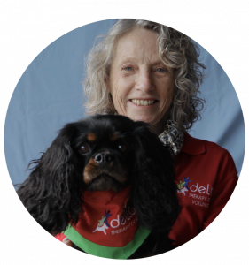 Smiling woman holding a black therapy dog wearing a Delta Society Australia bandana